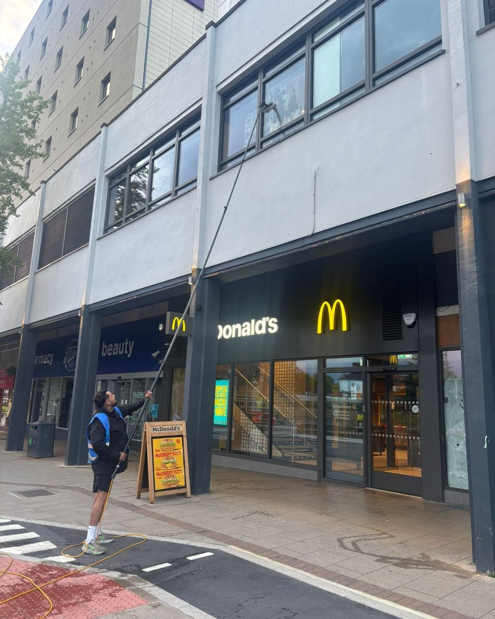 A window cleaner using a water-fed pole on the first-floor glazing above a row of shop units