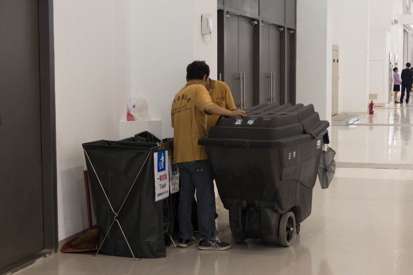 A member of cleaning staff moving wheeled waste carts through a bright, polished lobby